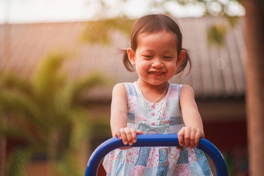 Happy Little Asian Girl Riding Seesaws at Outdoor Playground