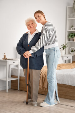 Healthy aging and home care support, young woman helping senior grandmother with walking cane in bedroom for family assistance and intergenerational bond