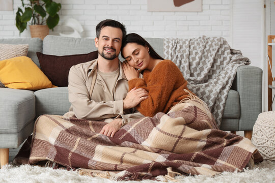 Relationship intimacy and comfort, happy couple relaxing at home under a warm blanket on the floor in a cozy living room interior