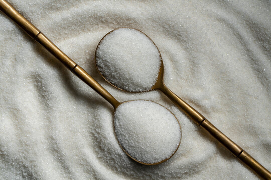 Top view of white refined sugar in two vintage golden spoons forming decorative pattern on heap of granulated sugar. Creative food concept for sweet ingredient or baking