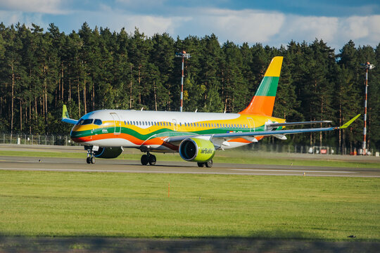Riga, Latvia - September 27, 2026: Colorful airBaltic passenger airplane with green, orange, and yellow livery taxiing beside a forested runway at an airport