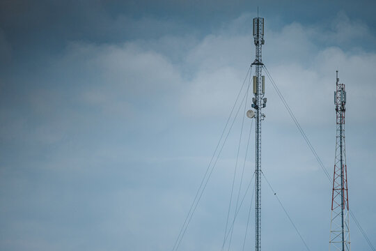 Tall telecommunications towers with antennas and support cables silhouetted against a cloudy blue gray sky in an outdoor infrastructure scene