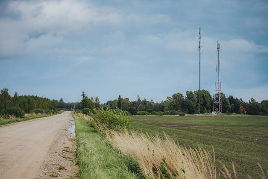 Rural dirt road beside cultivated fields and communications towers under a cloudy blue sky in a quiet agricultural countryside landscape