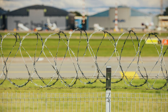 Coiled barbed wire fence with green grass and industrial buildings beyond, layered security barrier in an outdoor industrial perimeter landscape