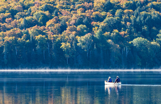 Two People on a White Canoe in a Calm Lake Surrounded by Fall Foliage