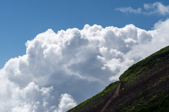 Hikers on a volcanic trail beneath a wall of cumulus cloud