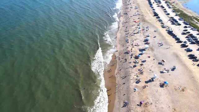 drone captures a bustling beach on Chincoteague Island, with swimmers near the water's edge.
