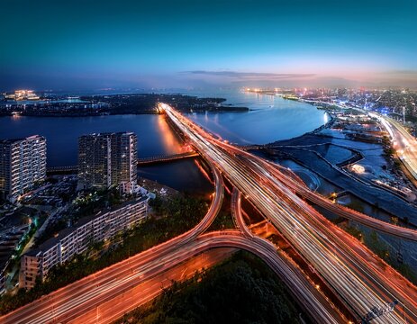 aerial night view of a busy highway with light trails from moving vehicles adjacent to a body of water and urban infrastructure