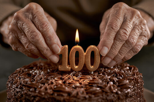 An extreme close-up of elderly hands carefully placing a single "100" shaped candle into the center of a chocolate cake.