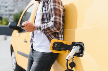 Fototapeta premium Deliveryman using smartphone while charging electric van