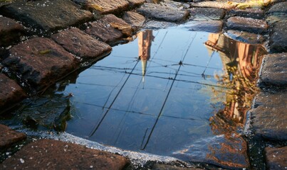 Fototapeta premium Reflection of church tower and trees in shallow puddle among cobblestones