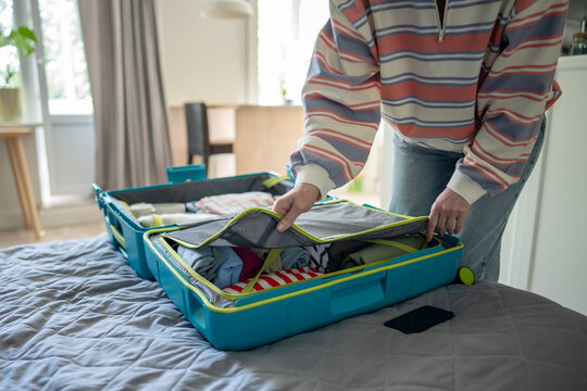 Woman traveler packing suitcase for holiday trip and covering neatly arranged items with divider, female hands zipping packed clothes and accessories in open luggage with mesh cover for safety.