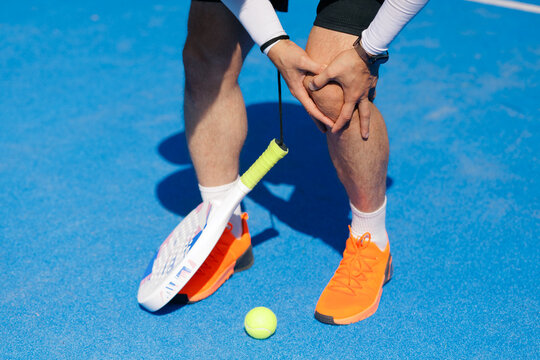 Padel tennis player holding injured knee during sports injury on court