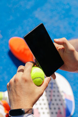 Fototapeta premium Padel player checking smartphone while holding tennis ball on court