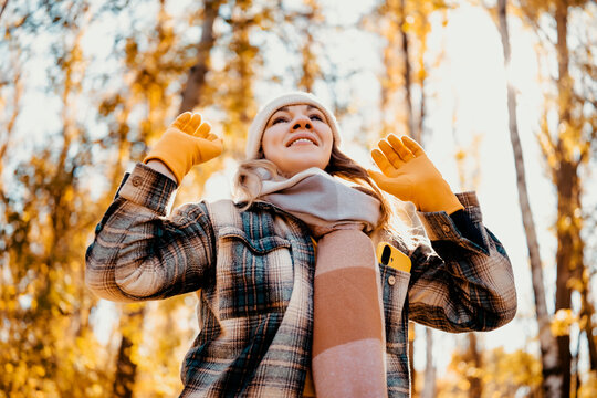 Joyful woman in autumn park raising hands &mdash; ultimate freedom concept. Cheerful hiker enjoying sunny forest weather. Seasonal outdoor recreation boosting mental health and vitality.