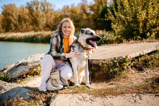 Smiling woman pet sitter embracing east european shepherd near water. Mutual trust and deep emotional bond between human and domestic animal. Young owner spending active weekend outside.
