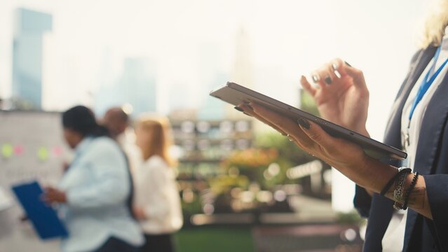 Businesswoman reads data from a tablet at an outdoor workspace with coworkers and a vision board, creating a collaborative professional setting for strategy, planning and project discussion.