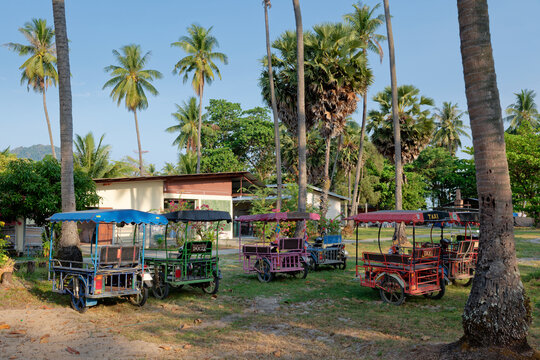 Row of colorful local sidecar motorcycle taxis parked under palm trees in Ko Muk