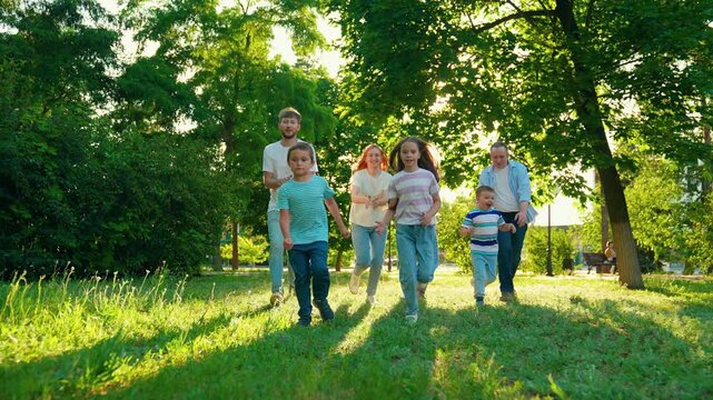Family parents dad mom, children kids son daughter enjoying outdoors. Family picnic with kids. Parents children playing on grass in park summer. Happy family running green grass in park. Slow motion