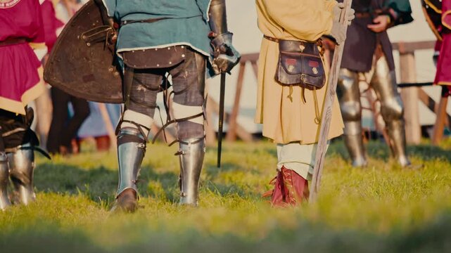 Knights finish tournament standing on green grass. Blurred warrior removes heavy metal armor in background after surviving exhausting historical combat event.