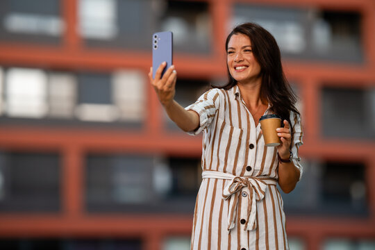 Woman taking selfie with smartphone holding coffee cup in city