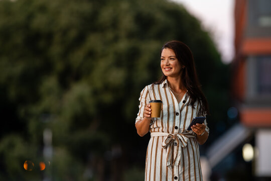 Smiling woman enjoying coffee walking in urban environment