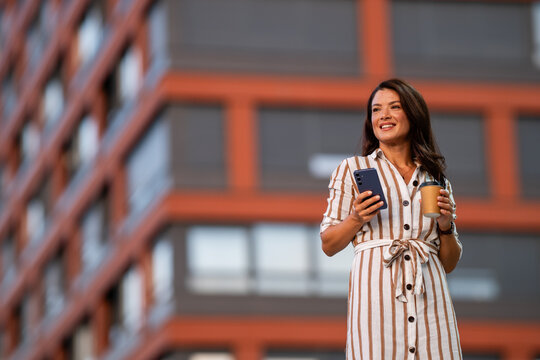 Professional woman using smartphone drinking coffee in city