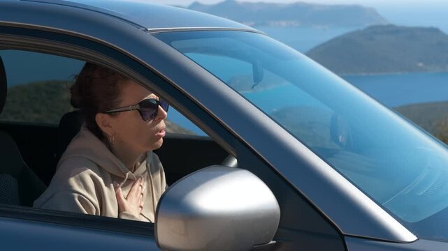 Asthmatic woman using inhaler during attack while driving. Anxious woman in a car experiencing a severe asthma attack, using an inhaler for relief while stopped on a mountain road with a beautiful sea