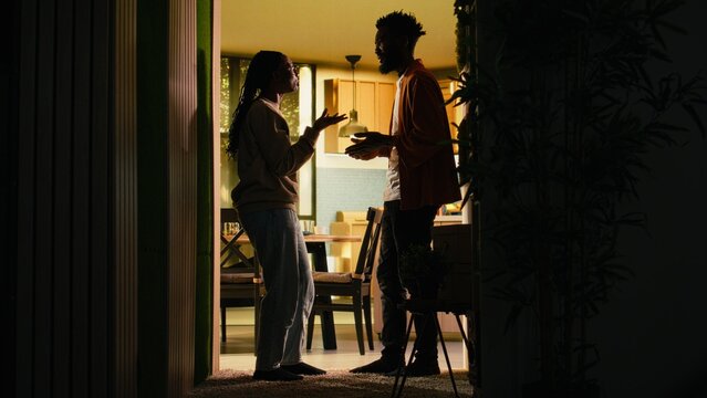 Black couple fighting at home in dark hallway looking furious and enraged during domestic quarrel; unhappy partners in conflict, toxic relationship due to constant heated argument and frustration.