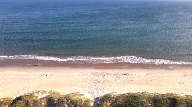 backward aerial reveal moves from Atlantic Ocean surf toward Outer Banks beachfront houses.