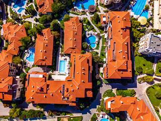 Resort architecture with red tile roofs and swimming pools. Aerial view shows multi story buildings featuring terracotta roofs and turquoise water pools surrounded by green trees.