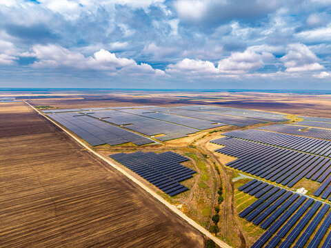 Wide aerial perspective of solar energy panels. Parallel rows of photovoltaic modules occupy rural flat terrain outdoors.