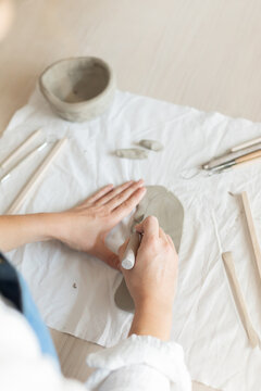 Women artist pottery shaping clay on a worktable with tools and cloth in a top-down perspective, focused and creative activity in crafting and production of handmade ceramics