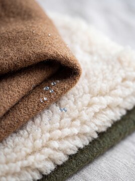 Water droplets on waterproof warm winter fabric stack including brown wool and white sherpa fleece textile texture