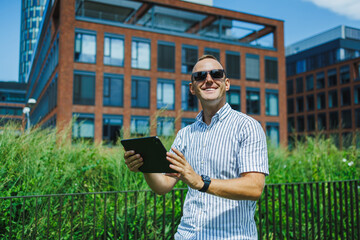Man uses tablet while standing outside in a modern urban area on a sunny day © DSMT