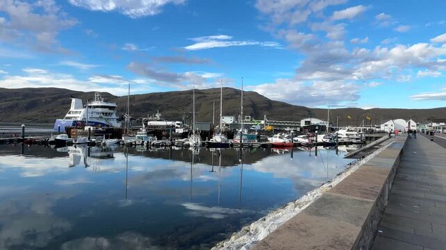 Boats moored in the quiet harbour, the water reflects the sky with the mountains in the background, Ullapool, Highlands, Scotland, United Kingdom