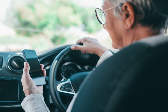 Senior woman driving a car and checking a mobile phone, representing the risks of distracted driving, smartphone addiction, and potential danger on the road