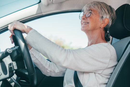 Happy mature woman driving confidently in her car while wearing glasses and a seatbelt, enjoying a sunny drive that conveys independence, safety and well-being for older adults.