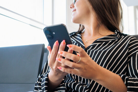 Woman engaging with her mobile phone, connecting with social media and digital content, smiling while sitting in an airport waiting area, enjoying travel and leisure time
