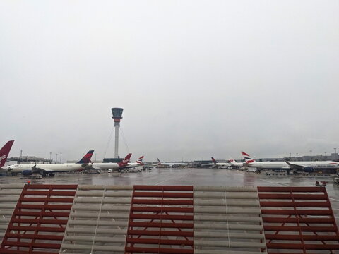 Commercial airplanes on the tarmac at Heathrow Airport with the control tower on a rainy London day