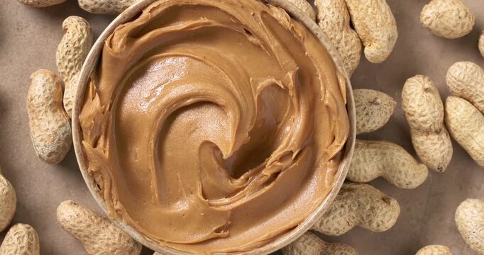 creamy peanut butter with a smooth decorative swirl on the surface, rotating on a rustic kitchen tabletop surrounded by scattered peanuts