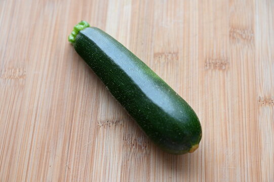 木目のまな板にのせた無農薬ズッキーニ1本 収穫したての夏野菜
