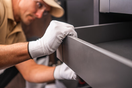 Gloved installer aligning a kitchen cabinet drawer