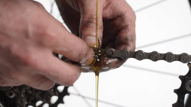 Mechanic lubricating a bicycle chain with oil in a studio setting against white background with components during maintenance mechanic applying lubricant