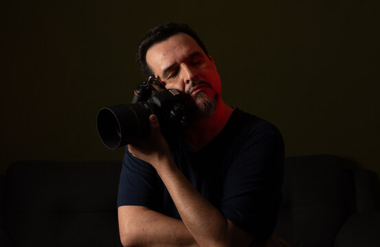 Male photographer holding camera with telephoto lens in dark studio