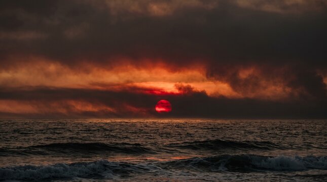 Dramatic red sun setting over turbulent ocean waves under heavy dark clouds, evoking El Nino conditions