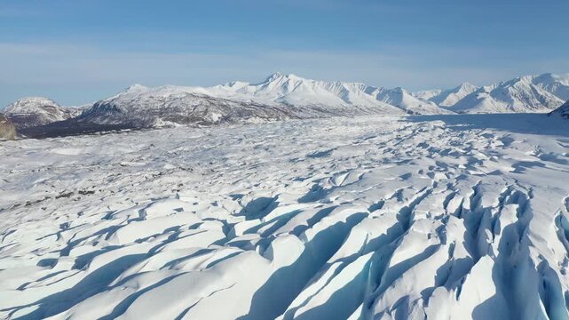 Drone Flyover Above Frozen Glacier Ice Fields with Scenic Mountain Backdrop