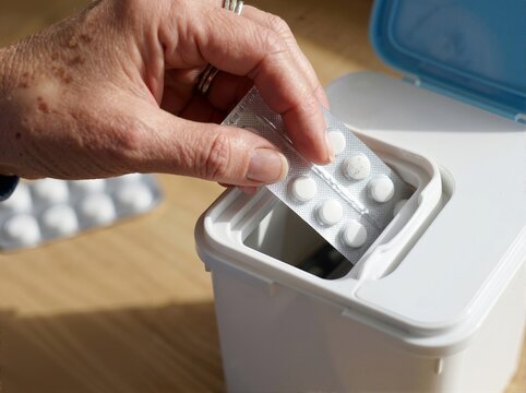 Senior person dropping blister pack of pills into disposal bin. Expired medicine return concept