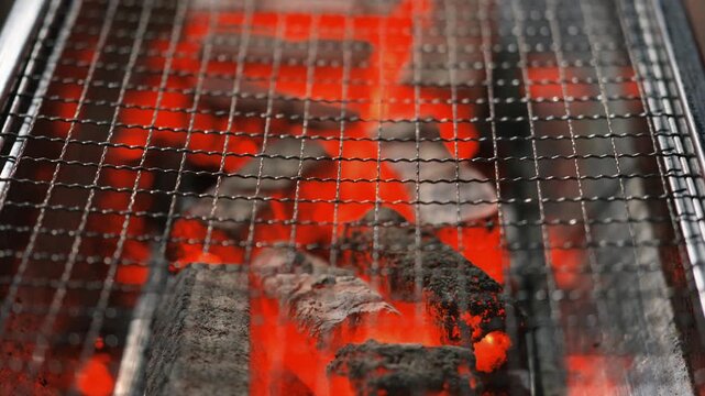 Glowing charcoal briquettes on metal grill grate
