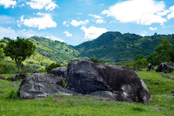 Large stone outcropping in a sunny rural pasture surrounded by green hills © Yeselly